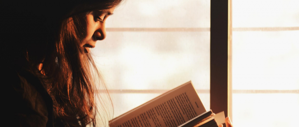 A girl reading in the light of a window
